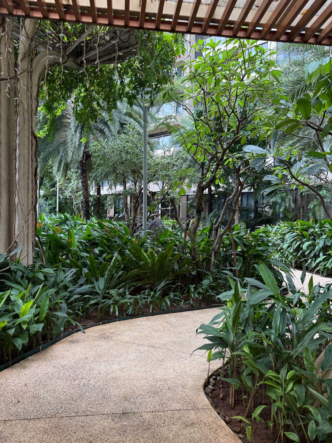 A planted walkway winding through dense greenery inside a residential development