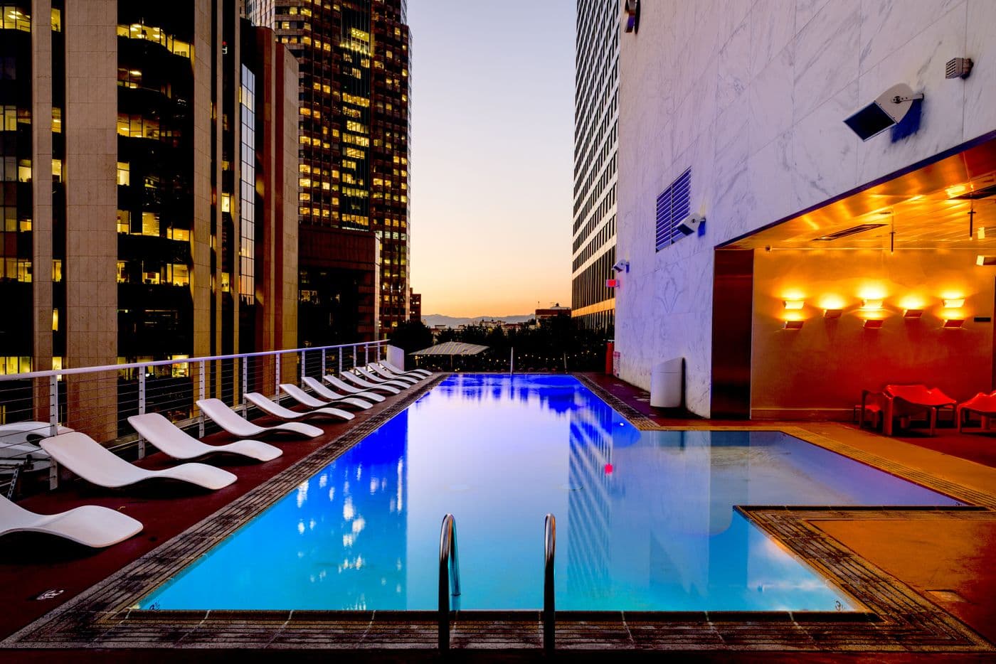A rooftop swimming pool lit at dusk, with loungers along one side